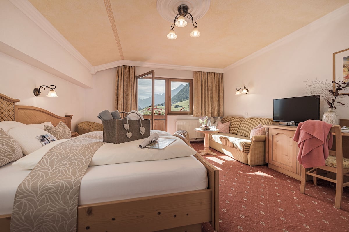 Quarto de hotel com cama, escrivaninha, televisão e janela com vista para as montanhas.