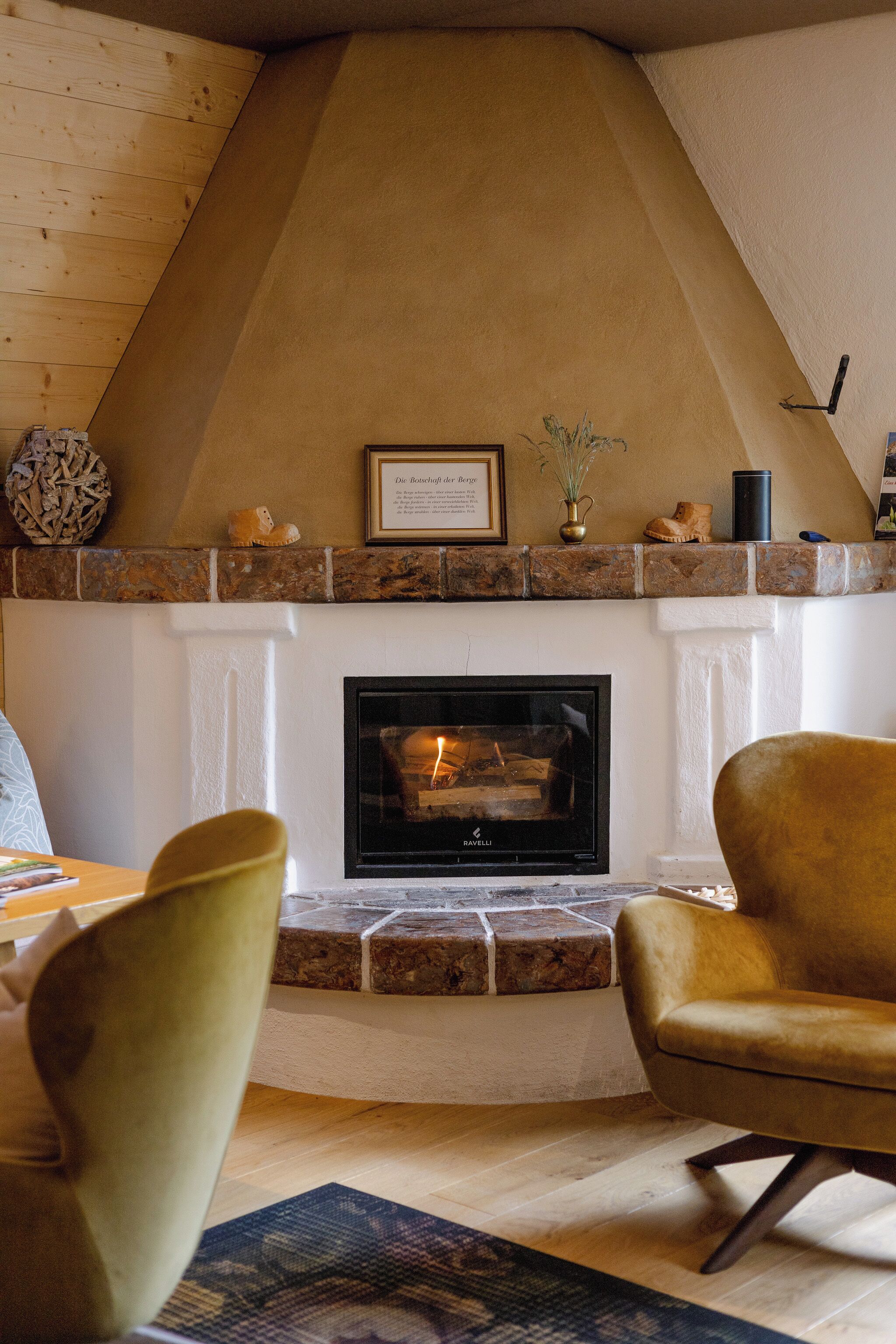 A fireplace with a stone mantle, a framed quote above it, and a vase with dried plants. There are two chairs in front of the fireplace.