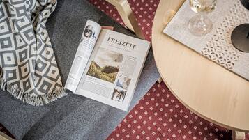 Una revista abierta sobre una mesa, con una manta estampada y una copa de vino.