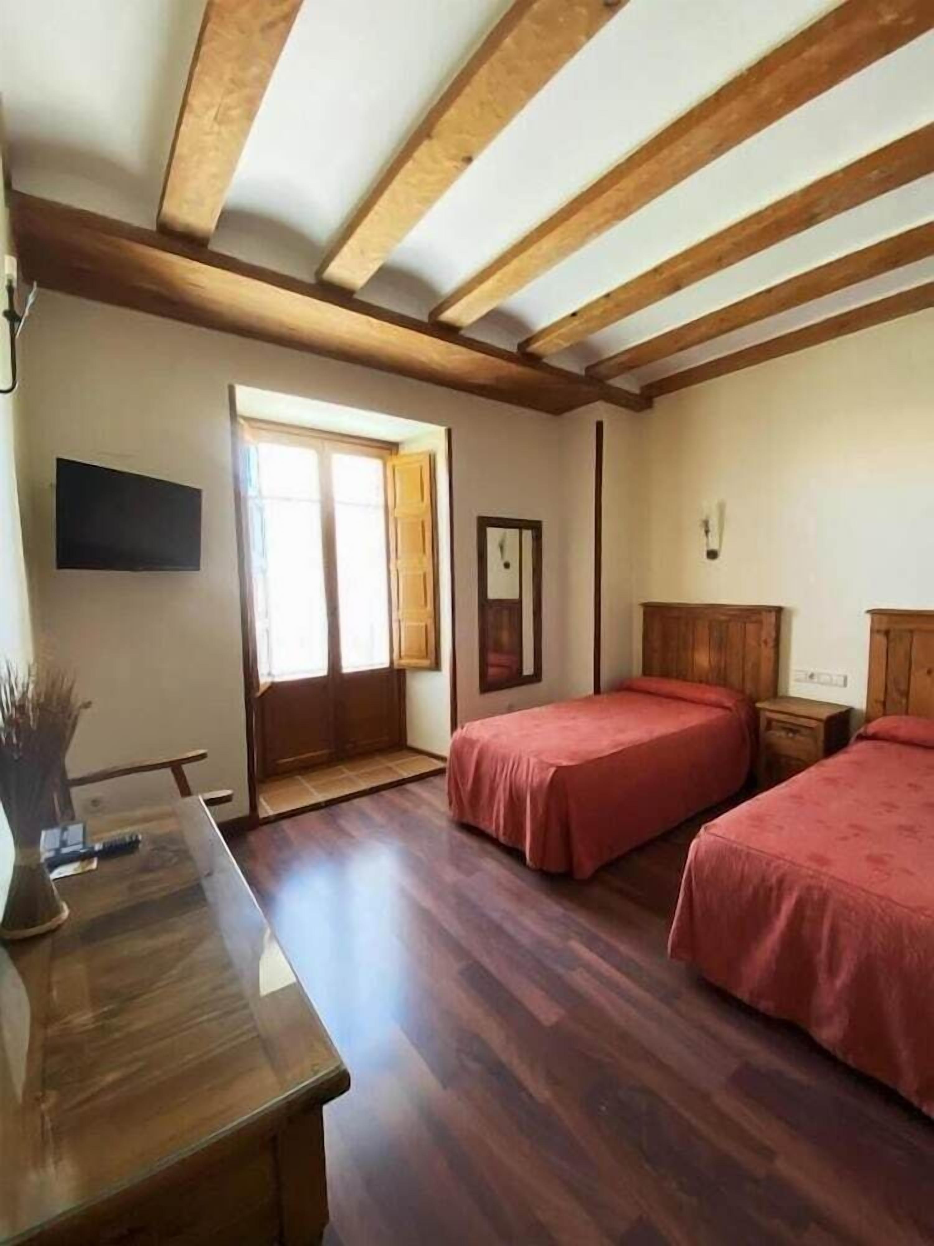Una habitación con dos camas, vigas de madera en el techo, un escritorio y una ventana.