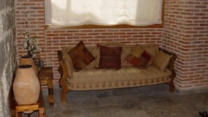 Ein gemütliches Zimmer mit Backsteinwand, einer gepolsterten Couch mit gemusterten Kissen, einem Holztisch und einem großen Fenster mit transparenten Vorhängen.