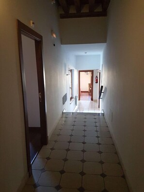 A hallway with a tiled floor, a door on the left, and a staircase leading to another room. - El Rastro (Avila)