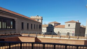 A courtyard with a brick floor and a metal railing, surrounded by historic buildings with stone walls and tiled roofs. - El Rastro (Avila)
