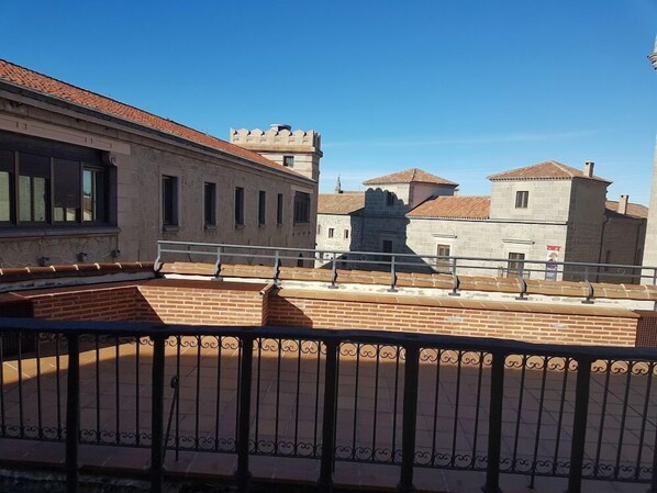 A courtyard with a brick floor and a metal railing, surrounded by historic buildings with stone walls and tiled roofs. - El Rastro (Avila)