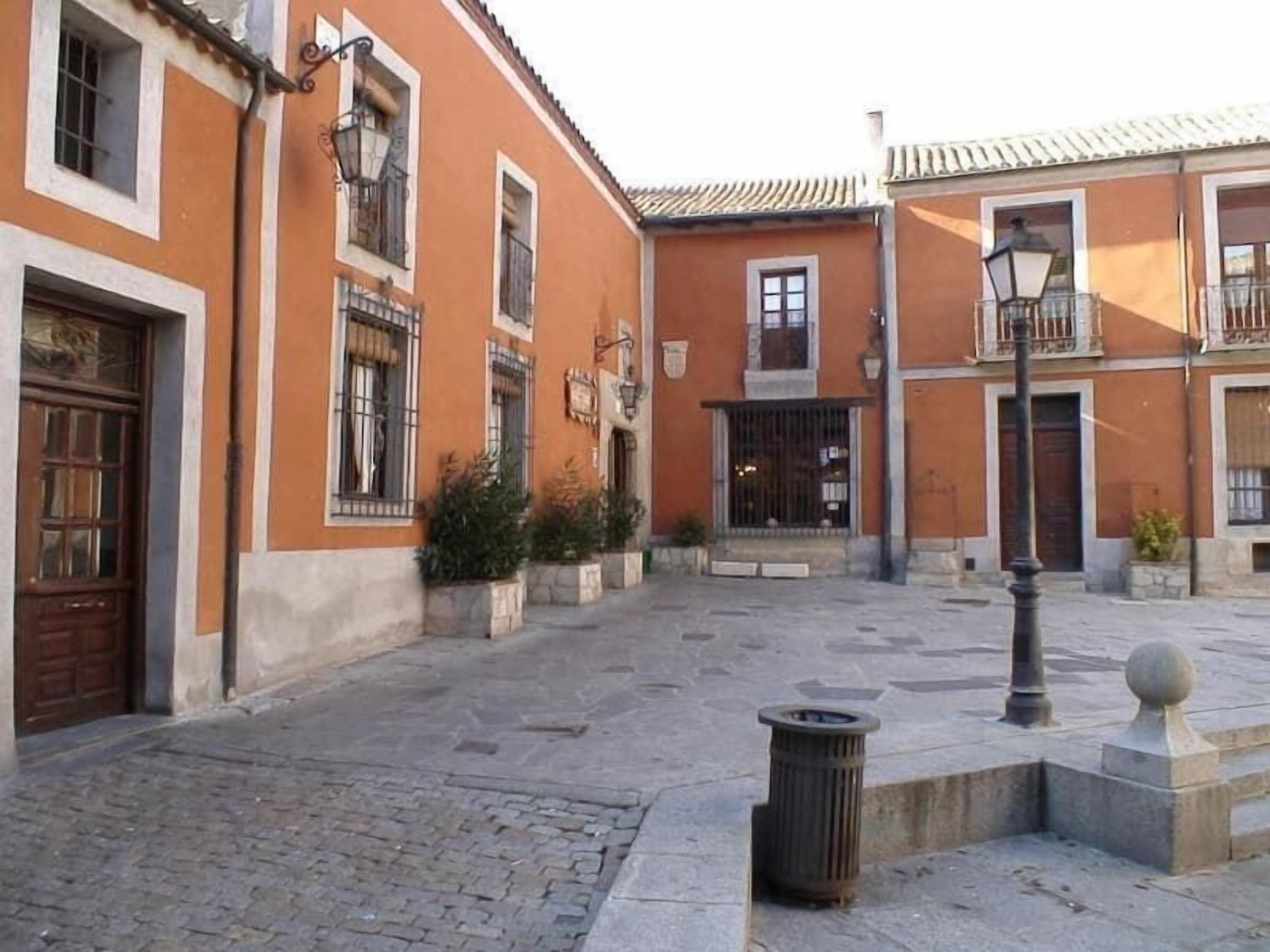 Un patio con pavimento de adoquines, edificios color naranja con ventanas de rejas y un bote de basura.