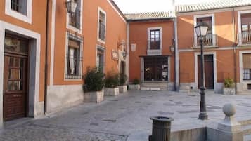 Un patio con pavimento de adoquines, edificios color naranja con ventanas de rejas y un bote de basura.