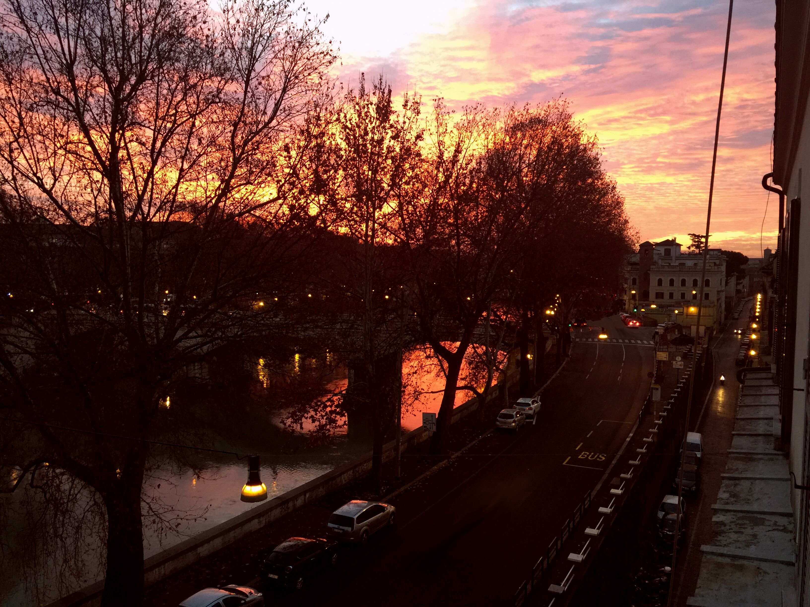 Vista del atardecer desde una ventana con vista a una calle de la ciudad, árboles y un río.