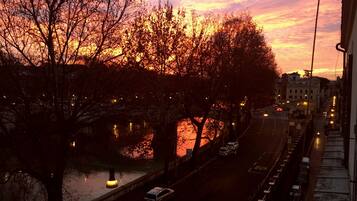 Vista del atardecer desde una ventana con vista a una calle de la ciudad, árboles y un río.