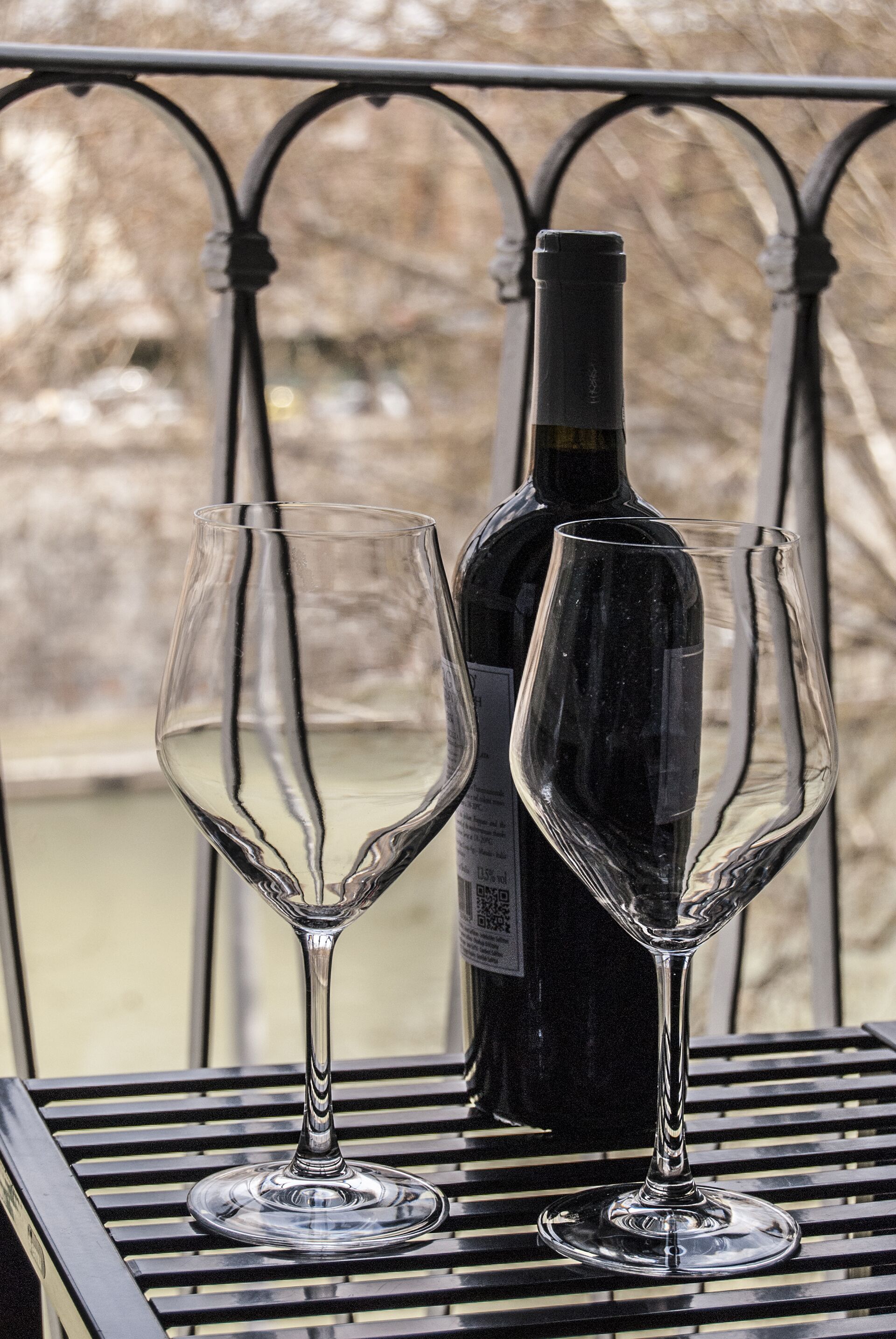 Two empty wine glasses and a bottle on a metal table with a metal railing in the background.
