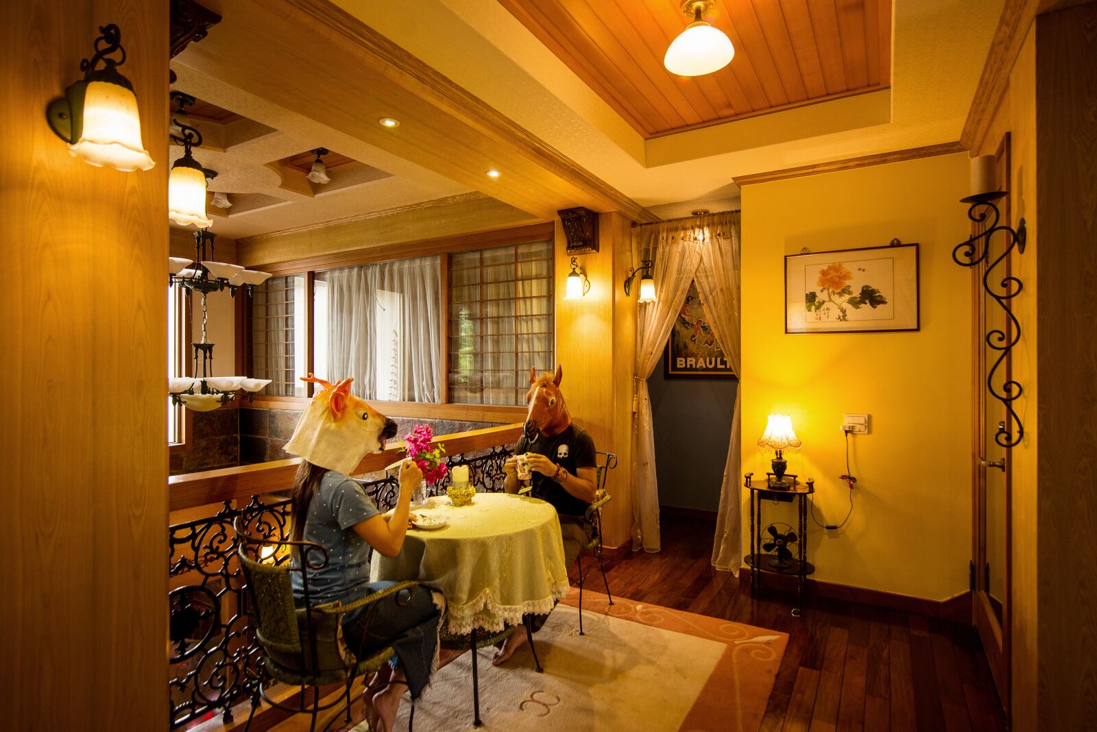 A dining area with a table set for two, a wooden ceiling, and a window with curtains.