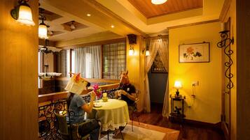 A dining area with a table set for two, a wooden ceiling, and a window with curtains.