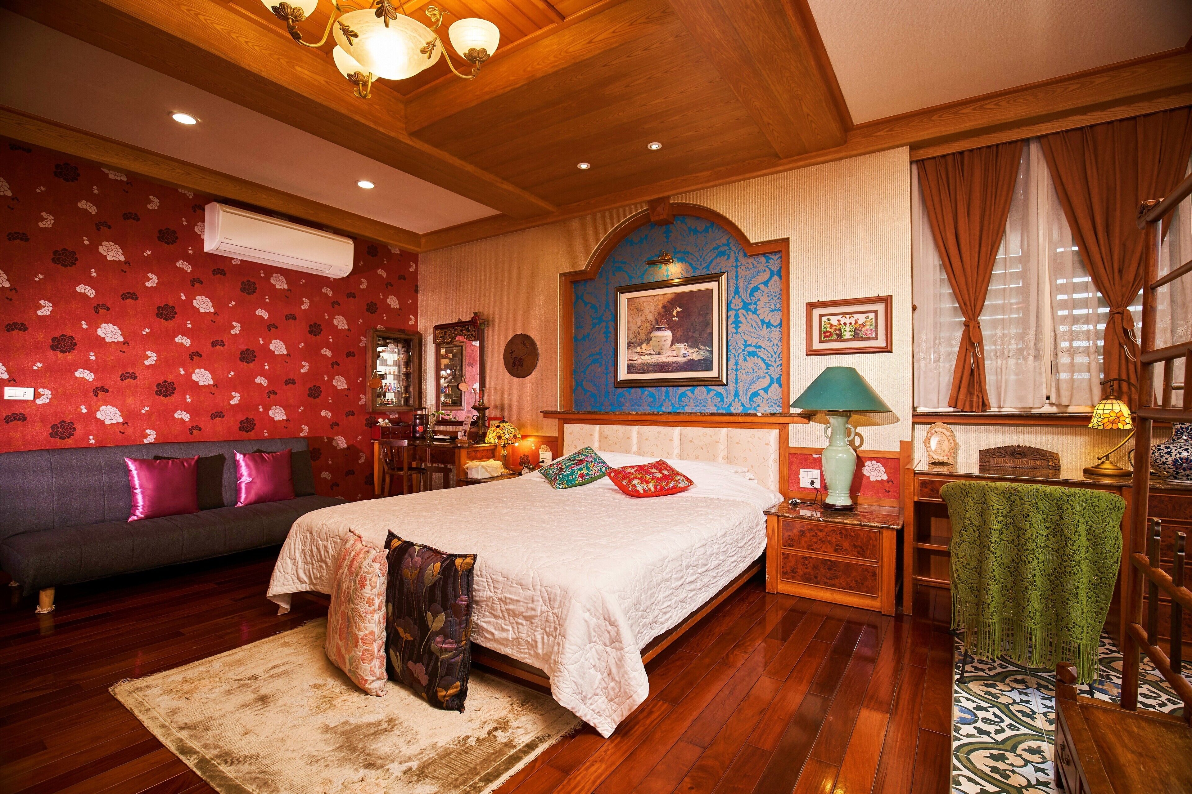 A bedroom with a large bed, a wooden ceiling, a red floral wall, and a green chair.