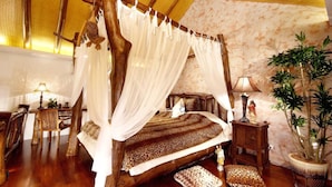 Una cama con dosel y mosquitera, muebles de madera, una mesita con lámpara y una planta en maceta.