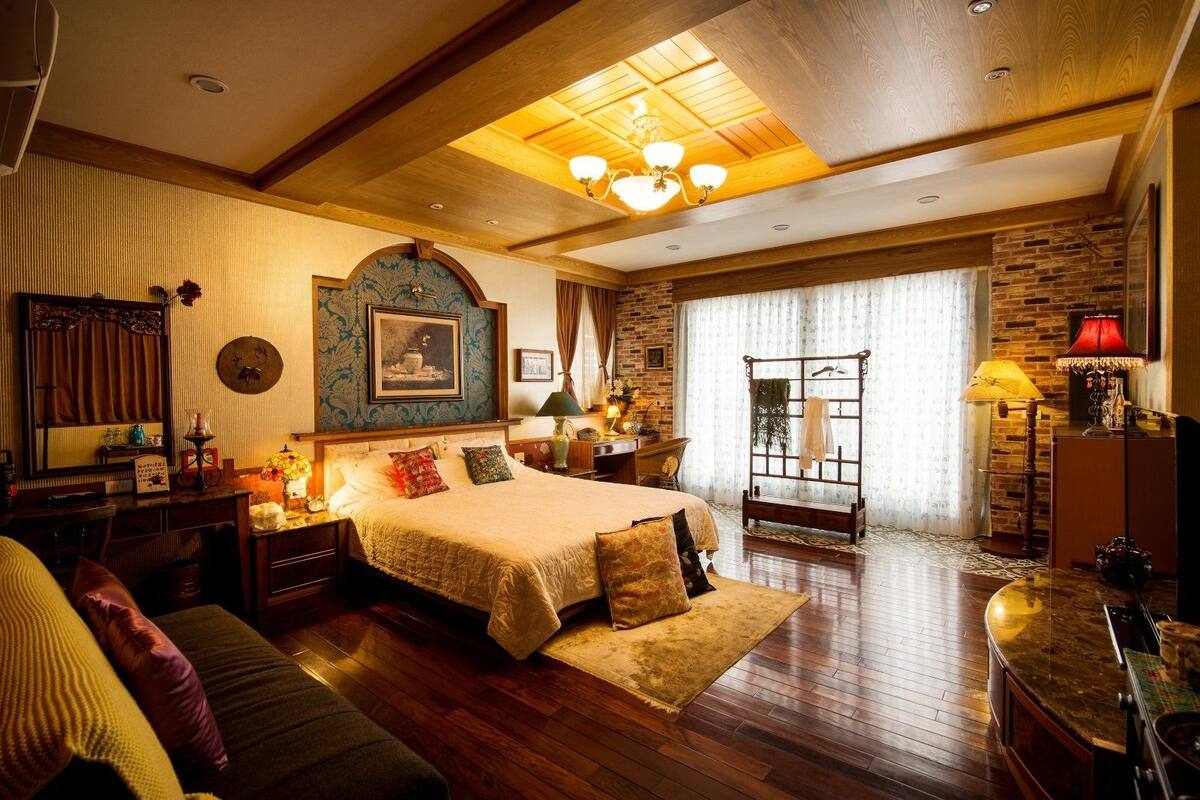 A spacious bedroom with a large bed, wooden flooring, a stone wall, and a chandelier.