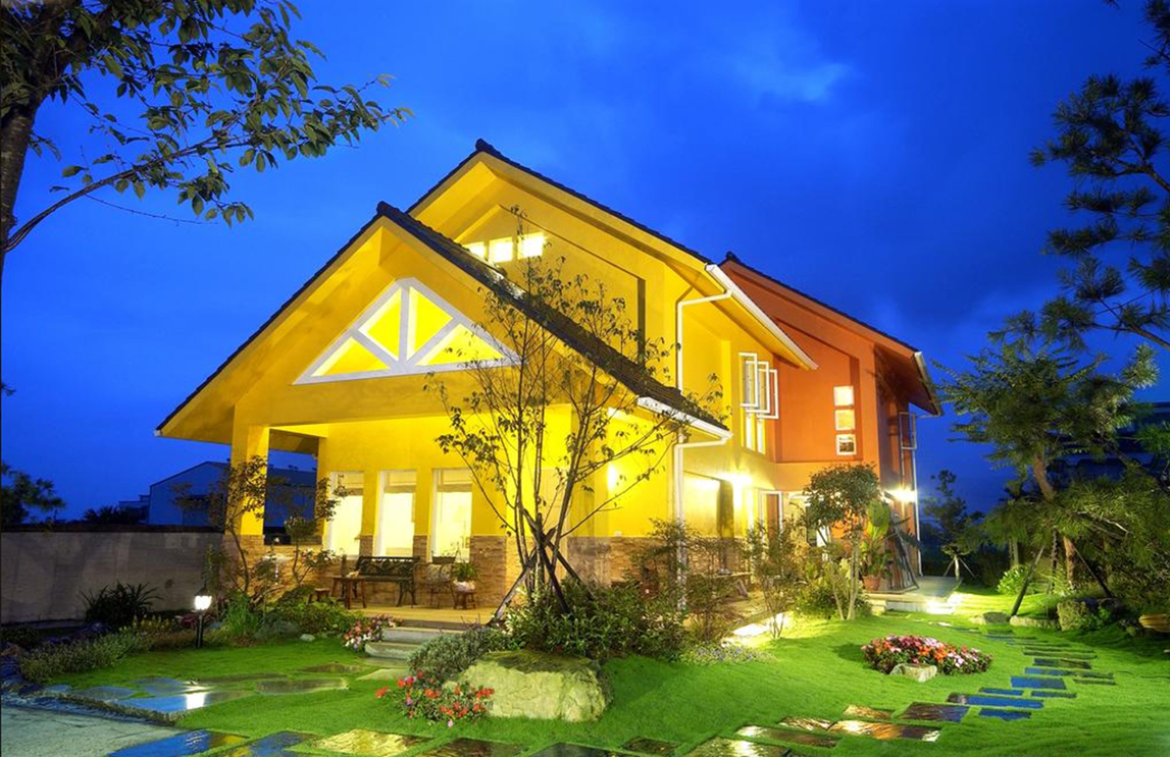 Uma casa moderna com fachada amarela e um jardim bem iluminado ao entardecer.