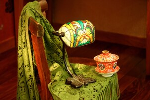 Uma cadeira de madeira com assento e encosto de crochê verde, uma borboleta de metal decorativa e um abajur de vitral colorido.