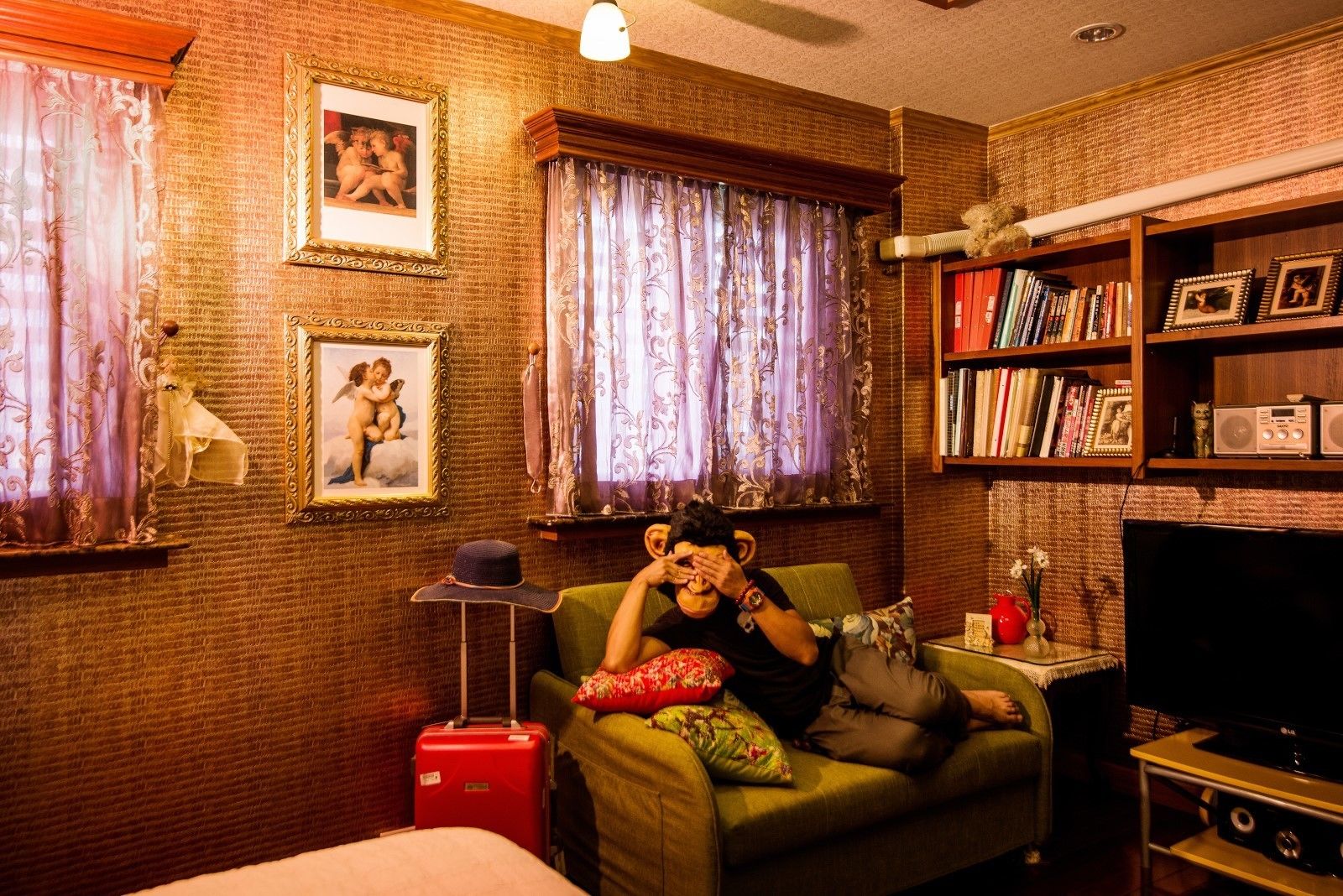 A cozy living room with a green sofa, a red suitcase, and a bookshelf filled with books and decorative items.