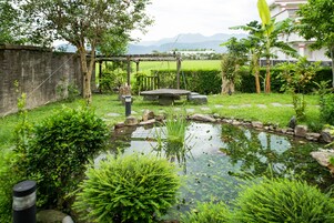 Un jardín con un estanque, asientos de piedra y una pérgola.