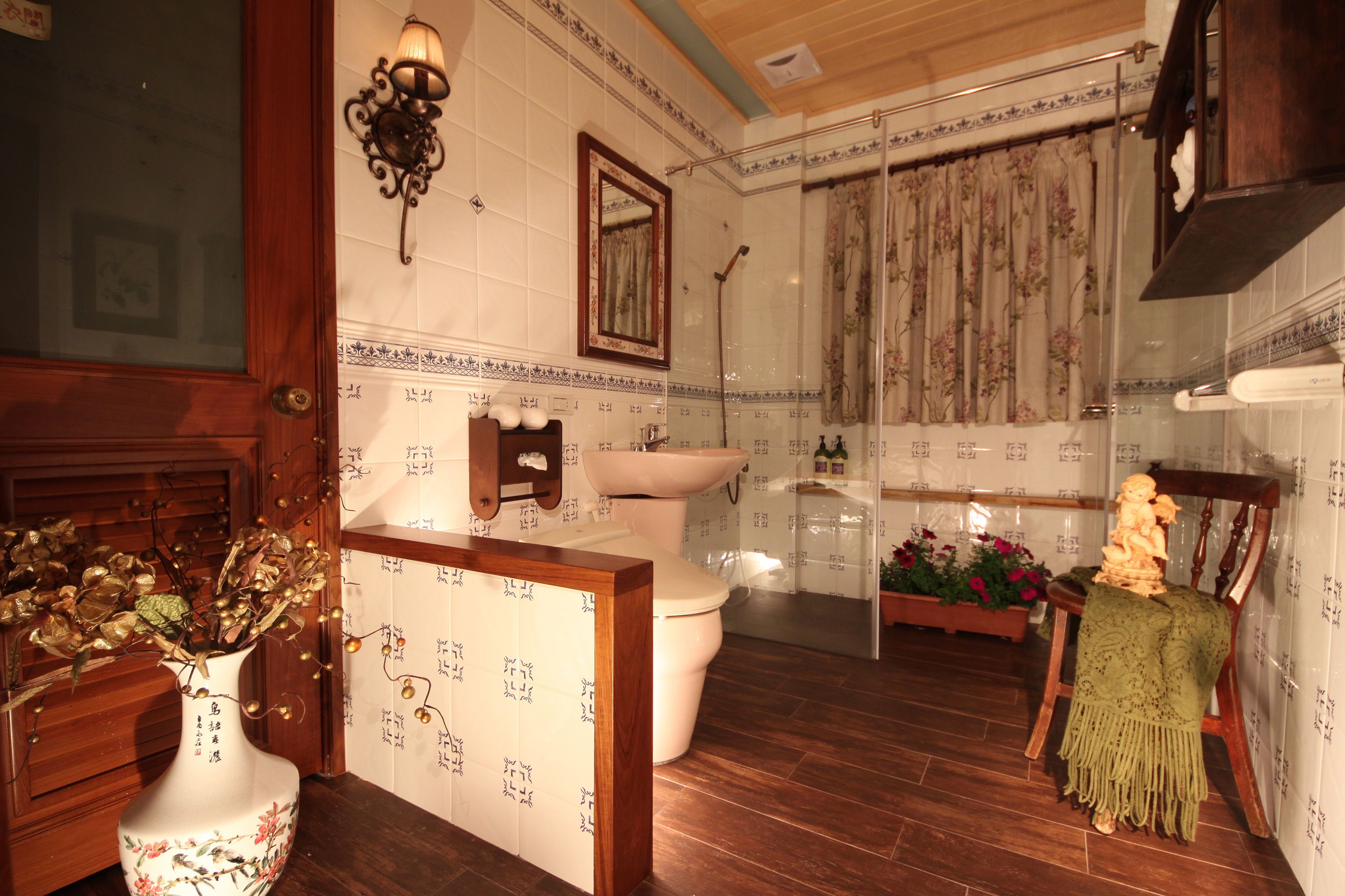 Une salle de bain avec un meuble-lavabo en bois, des toilettes, un lavabo, une douche et un vase décoratif contenant des fleurs séchées.