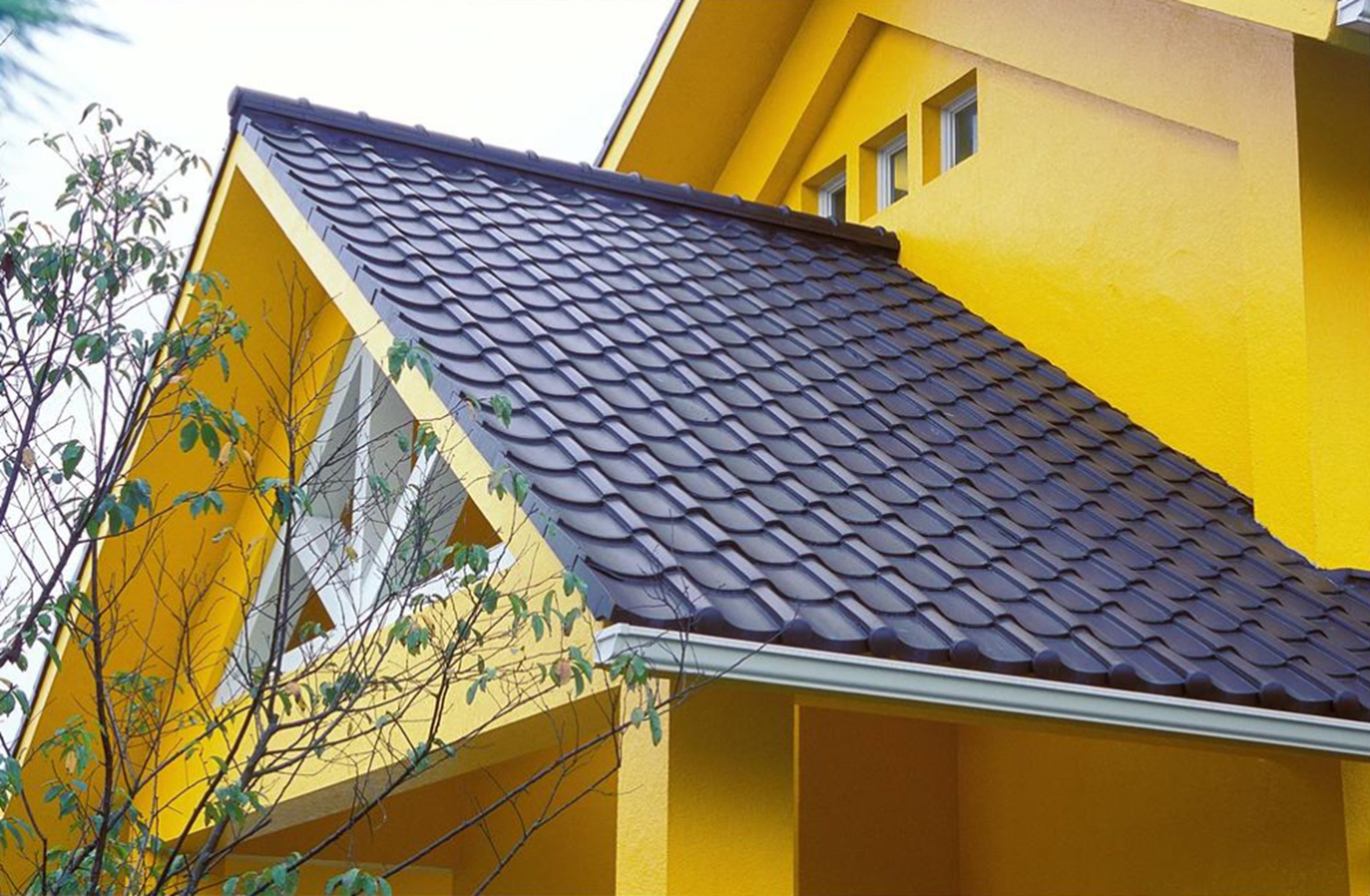 A yellow building with a dark tiled roof and a window.