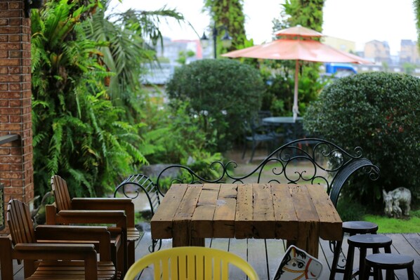 A wooden table and chairs on an outdoor patio with a brick wall, surrounded by lush greenery and a statue. - The Dew B&B (Dongshan)