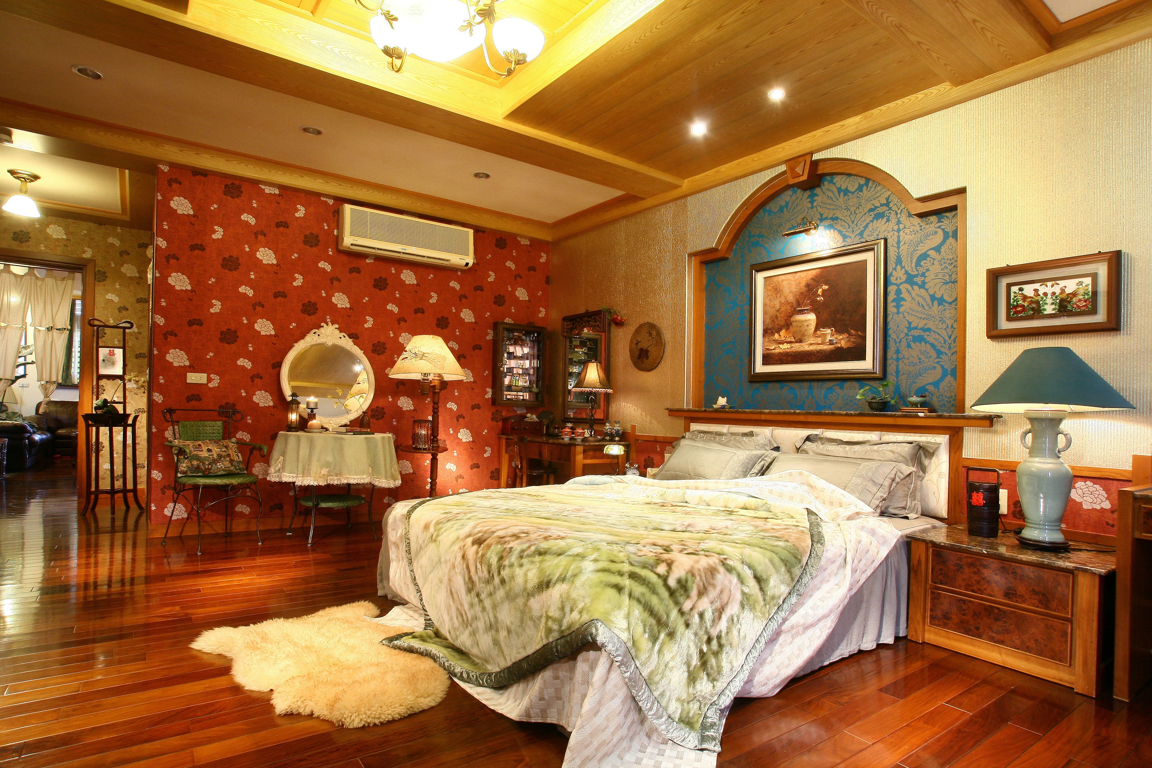 Une chambre à coucher de style traditionnel, avec un grand lit, un plancher en bois, un miroir et une commode.