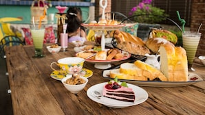 Una mesa de madera con varios alimentos, como pan, pasteles y una rebanada de pastel, junto con varias bebidas.