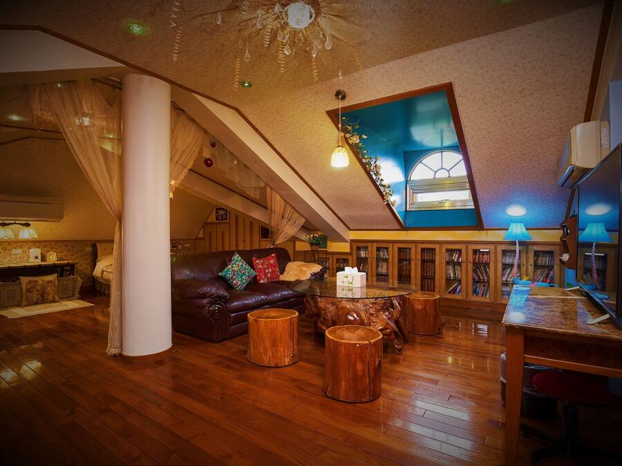 A spacious loft with a high ceiling, wooden flooring, a leather sofa, and a large window with a view.