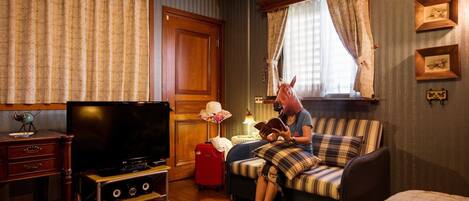 A cozy room with a television, a red suitcase, a striped sofa, and a person reading a book.