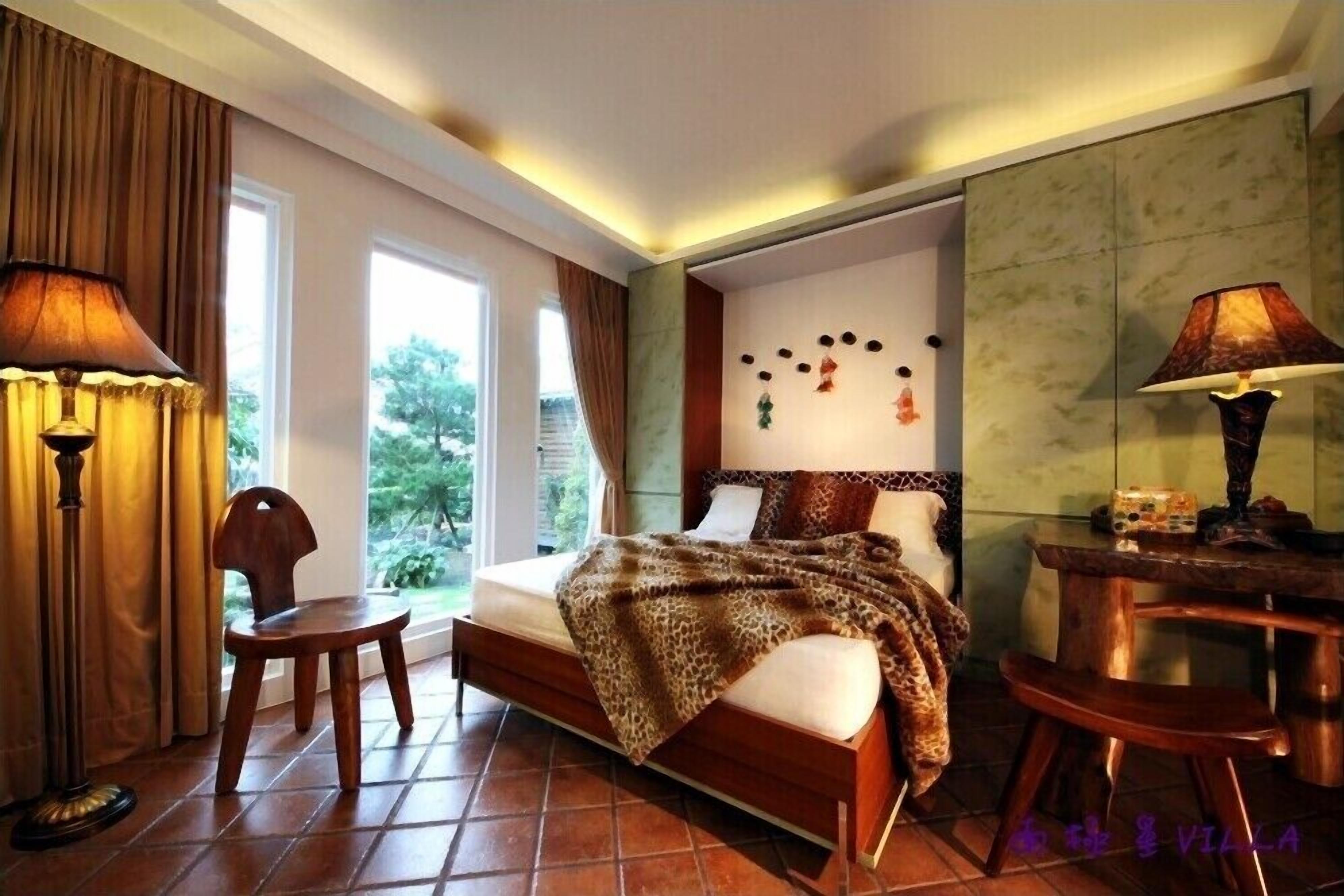 A bedroom with a bed, a desk, a chair, and a window with curtains.