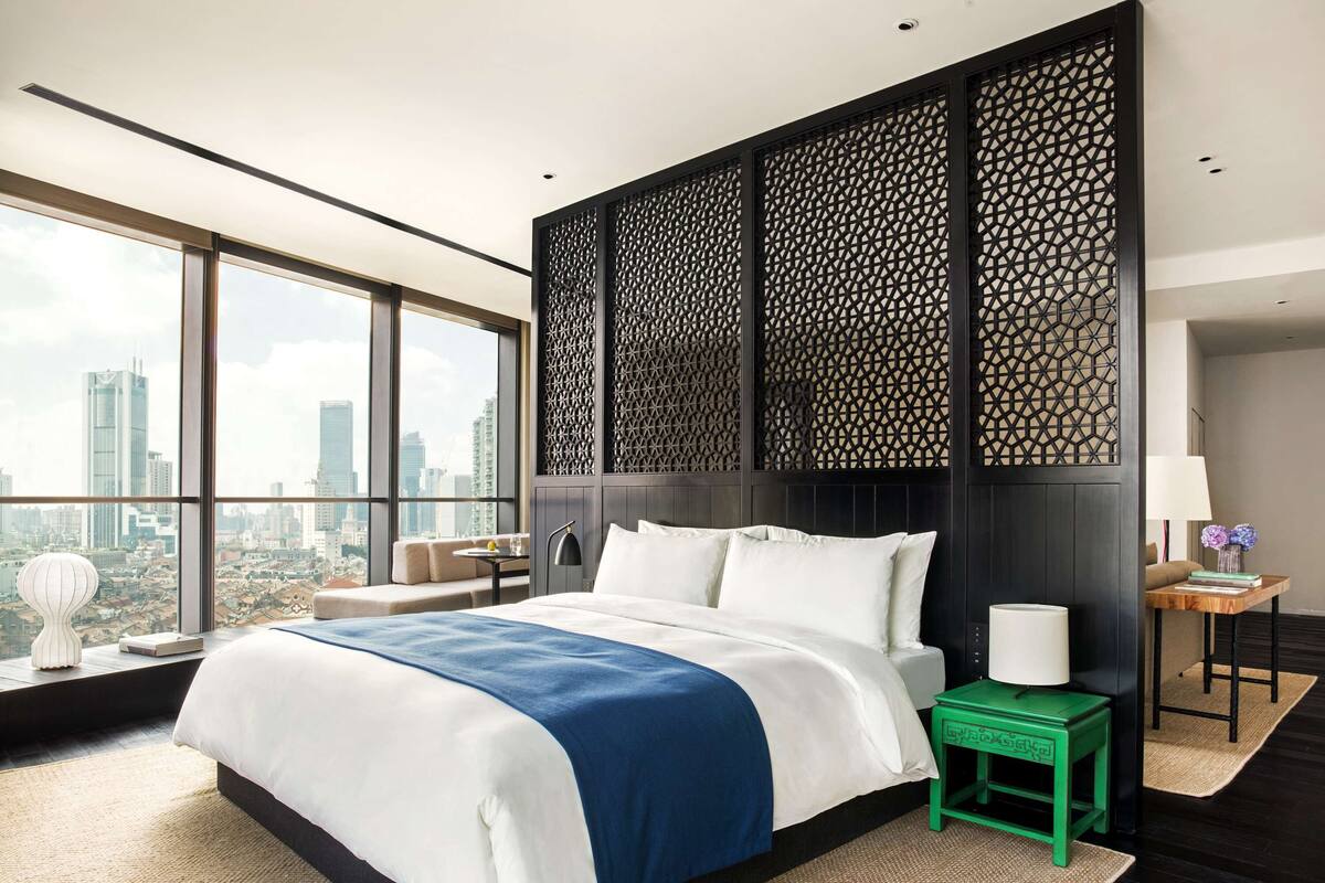 Ein modernes Hotelzimmer mit einem großen Bett, Blick auf die Stadt und einer dekorativen Wandverkleidung.