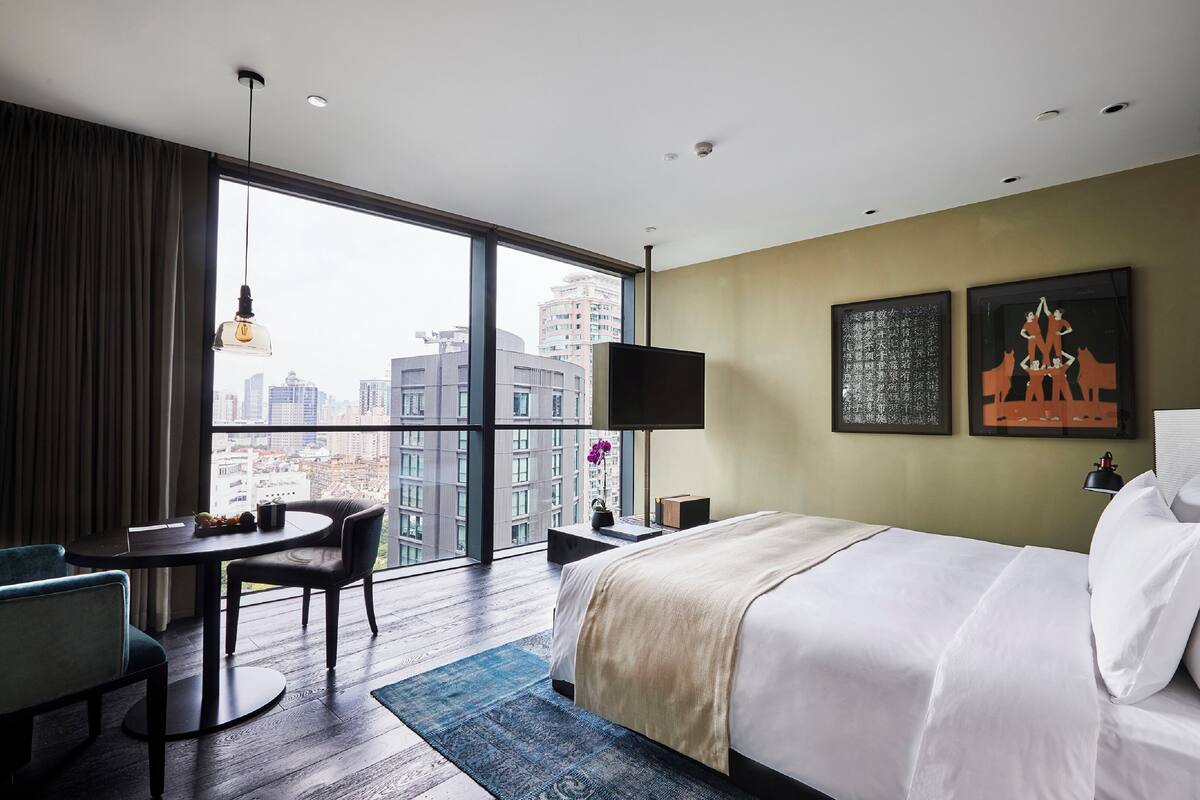 Ein Hotelzimmer mit großem Fenster, einem Bett, einem Schreibtisch und einem Sessel.