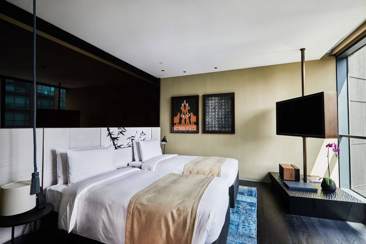 Ein modernes Hotelzimmer mit einem großen Bett, einem Flachbildfernseher, einem Schreibtisch mit Lampe und Kunstwerken an den Wänden.