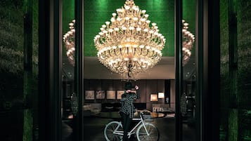 A modern interior with a large chandelier, a bicycle, and a person adjusting their hat.