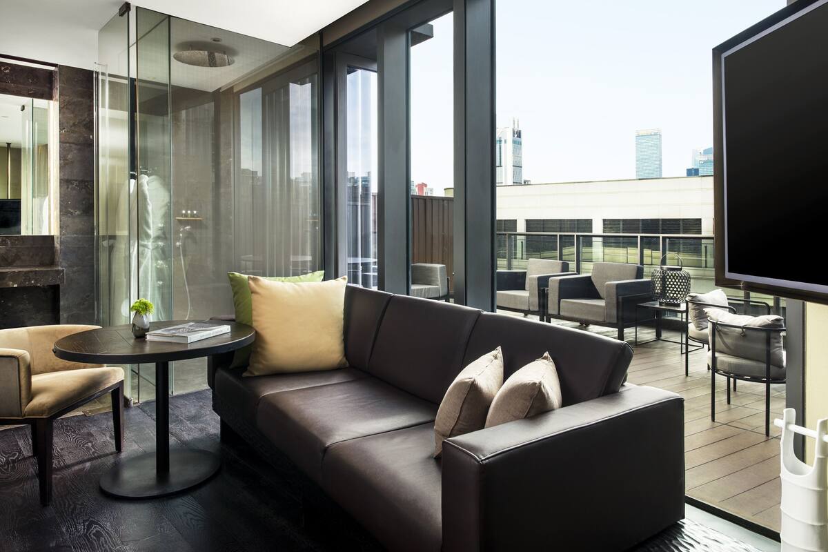 Ein modernes Wohnzimmer mit einer Couch, Sesseln, einem kleinen Tisch und einem großen Fenster mit Blick auf die Stadt.