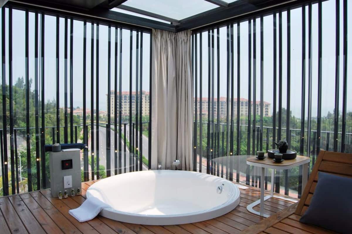 Un balcon avec un jacuzzi, une petite table avec un service à thé, et une vue sur les bâtiments et la verdure.
