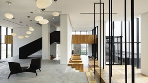 Un vestíbulo amplio con una escalera moderna, sillas negras e iluminación colgante.