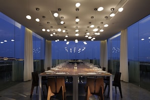 Un salón de conferencias con una larga mesa dispuesta para una reunión, ventanas amplias y vistas a la ciudad.