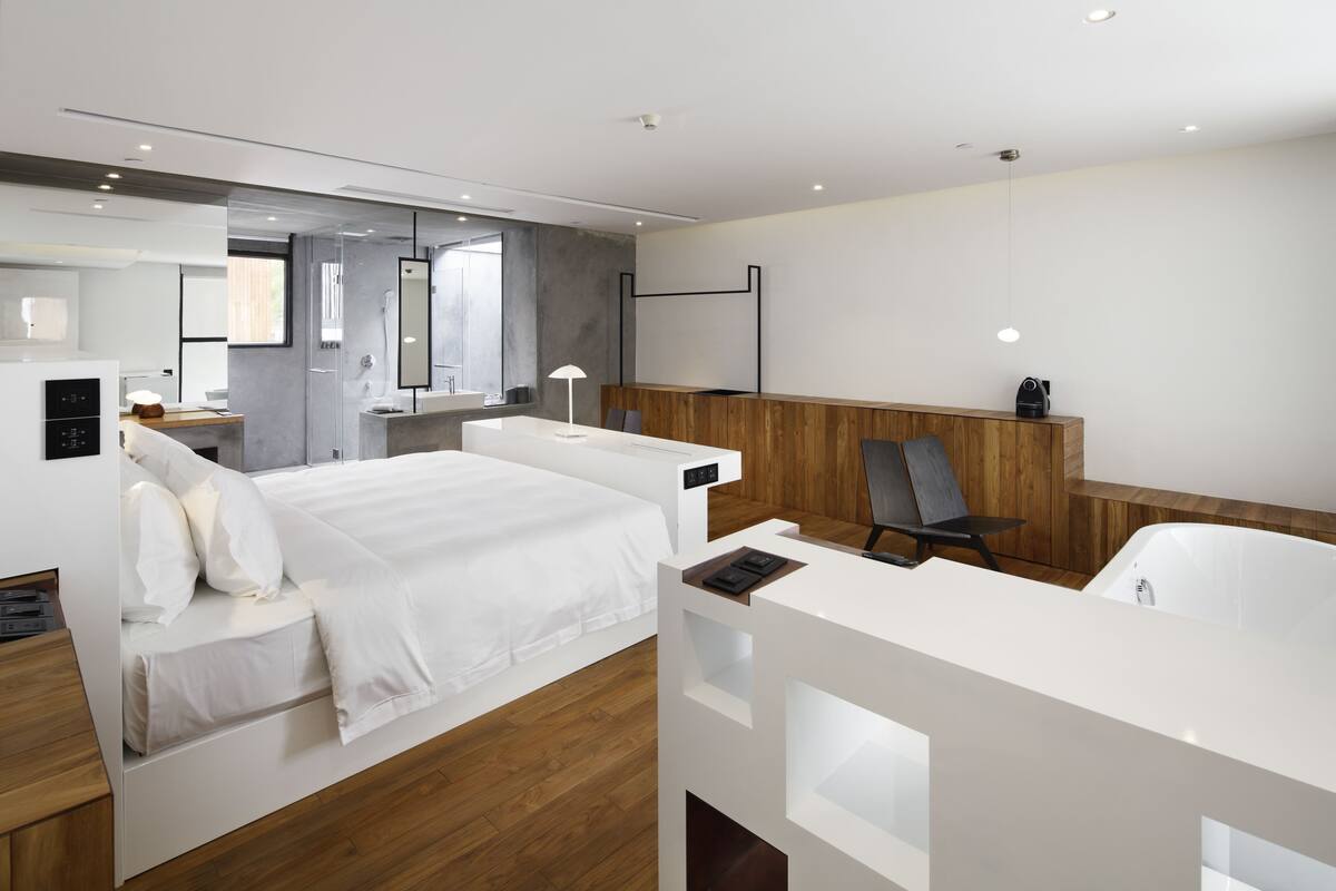 Une chambre d’hôtel moderne dotée d’un grand lit, d’un bureau, d’une chaise, d’un espace douche et d’un mur décoratif en bois.
