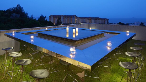 Una terraza en la azotea con una mesa cuadrada en el centro, rodeada de taburetes de bar y velas.