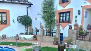 Une table en forme de baril, faite de bois, sur laquelle se trouve une assiette de nourriture, deux verres à vin et une bouteille de vin, le tout placé dans une cour avec une piscine et des plantes en pot.