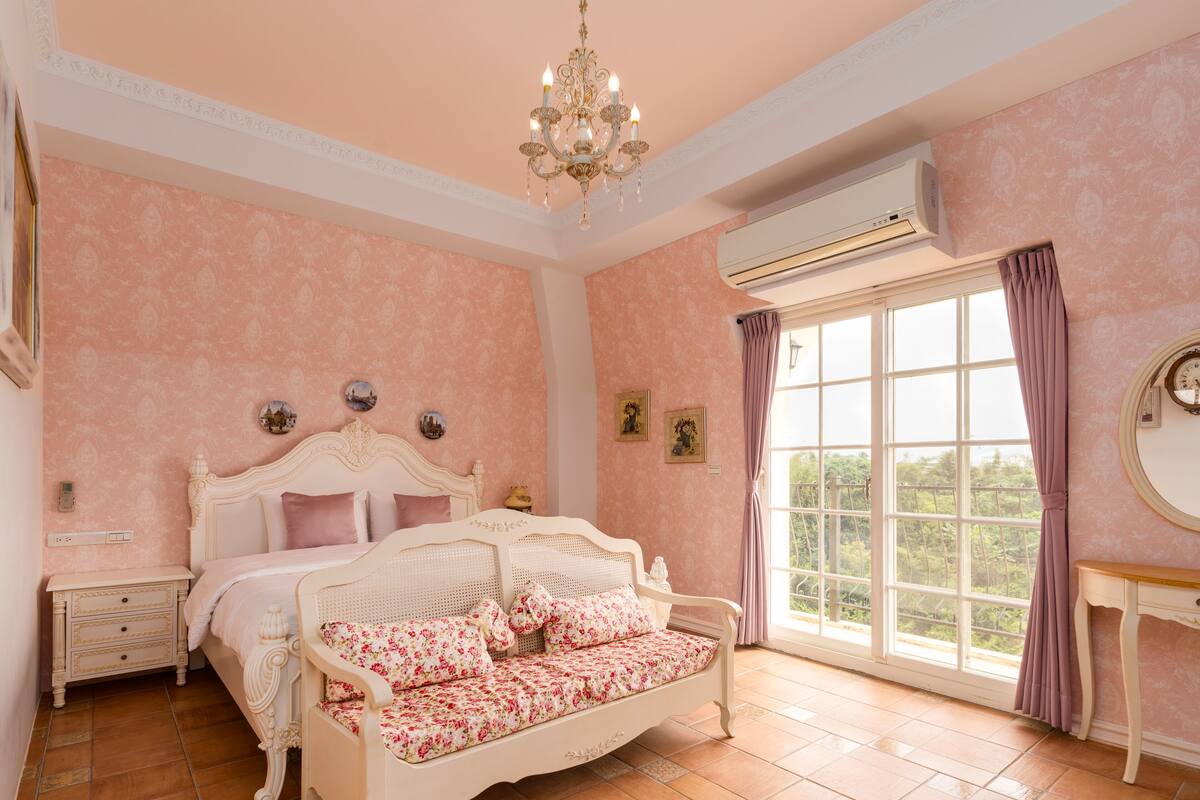 Un dormitorio con una cama grande, una mesita de noche, un aparador, una ventana con cortinas y un equipo de aire acondicionado.