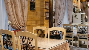 Un coin repas chaleureux avec des murs en bois, des rideaux à motifs floraux et une table entourée de chaises.