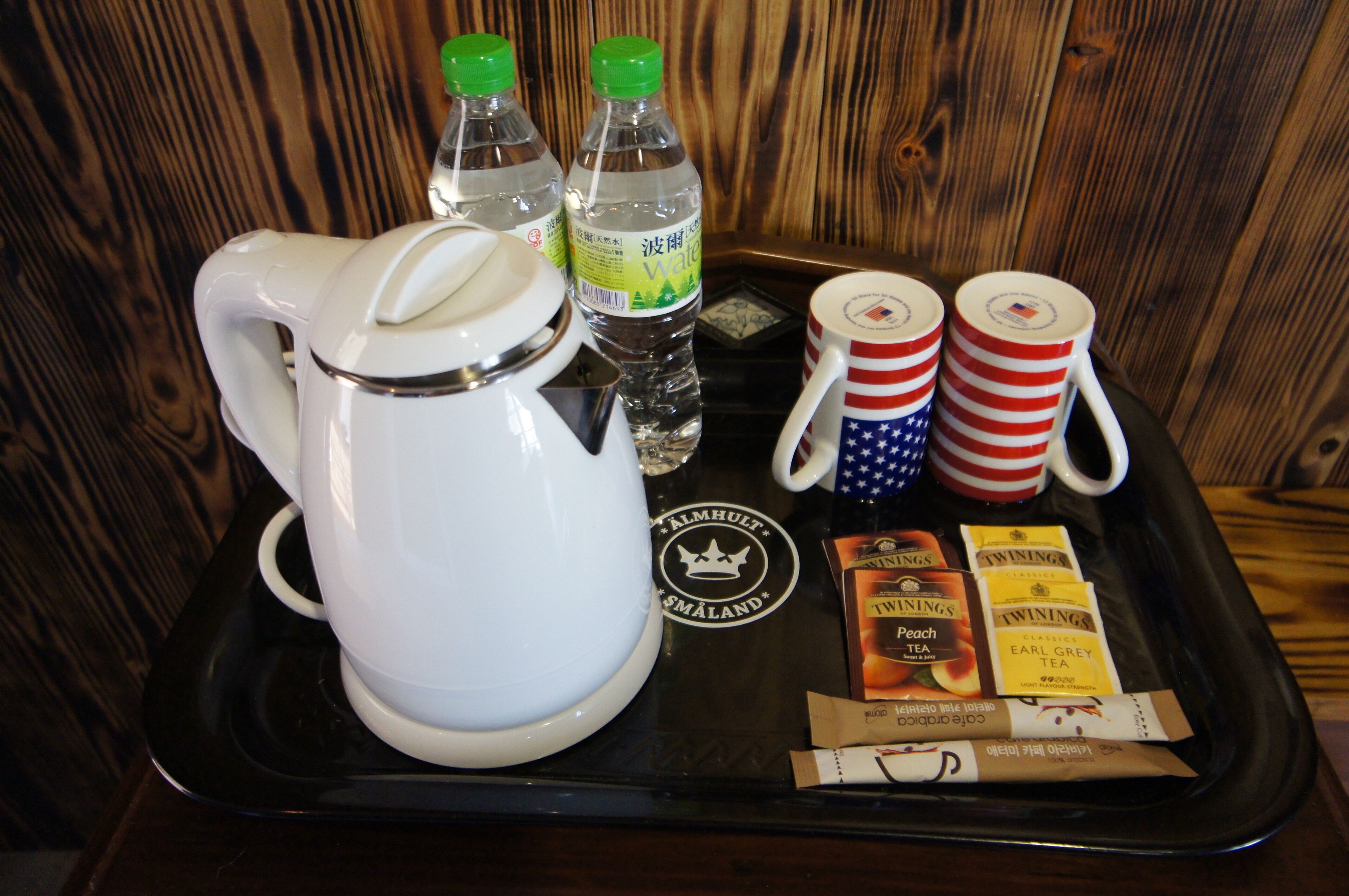 Una bandeja con una tetera blanca, dos botellas de agua, dos tazas con diseños de la bandera estadounidense y sobres de té Twinings.