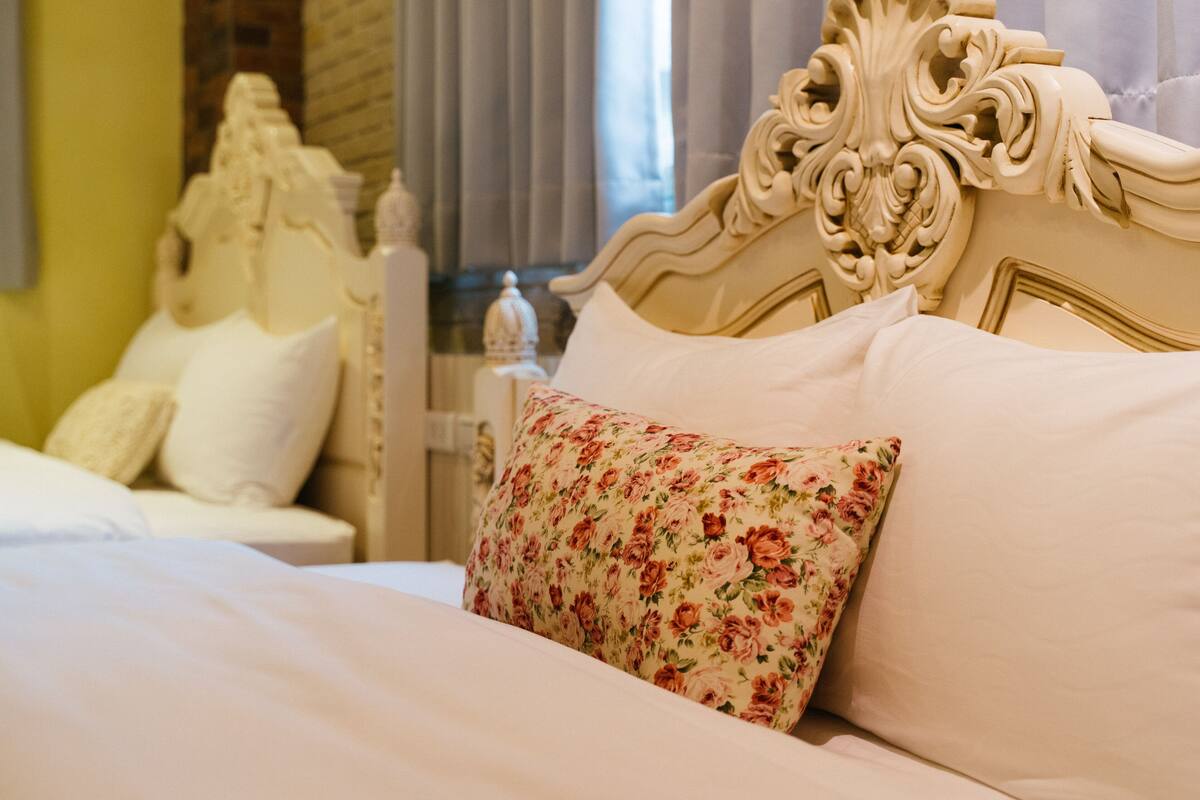 Una cama con un cojín estampado, un cabecero blanco y una mesita de noche con una lámpara.