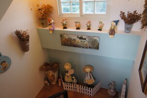 Una habitación con ventana, una estantería con adornos, una valla de piquetes blancos y un cuadro.