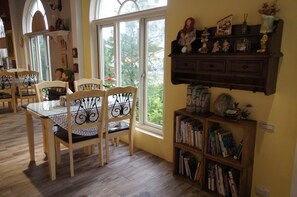 A dining area with a table and chairs, a bookshelf with books, and a window with a view of trees. - Brulees Done (Dongshan)