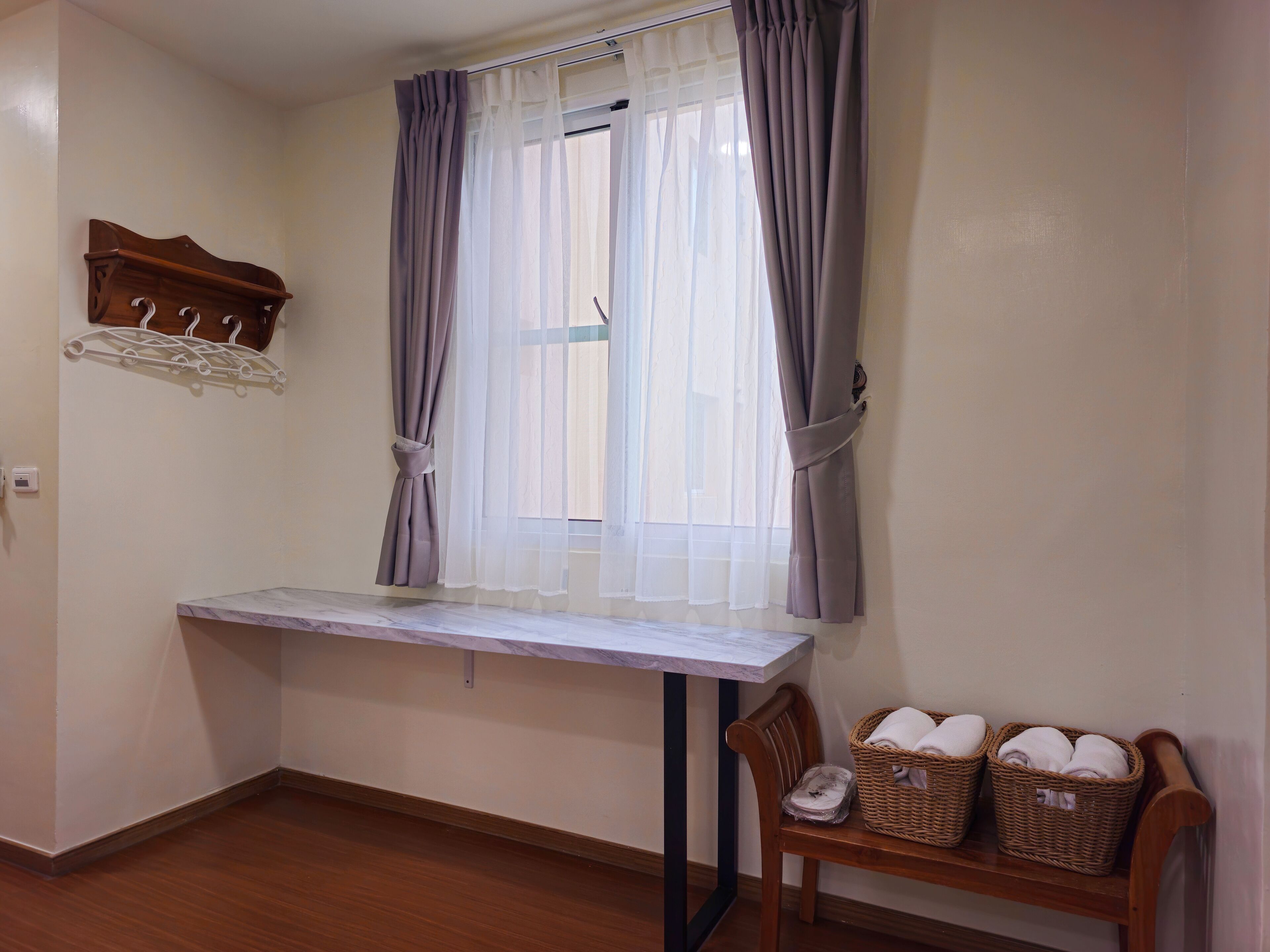 A room with a window, a table, a chair, and two baskets on a bench.