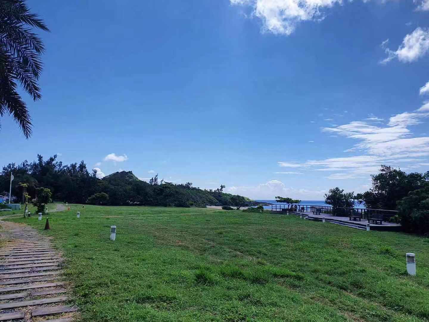 Un campo cubierto de césped con un sendero de madera que lleva a una edificación con vistas al mar.
