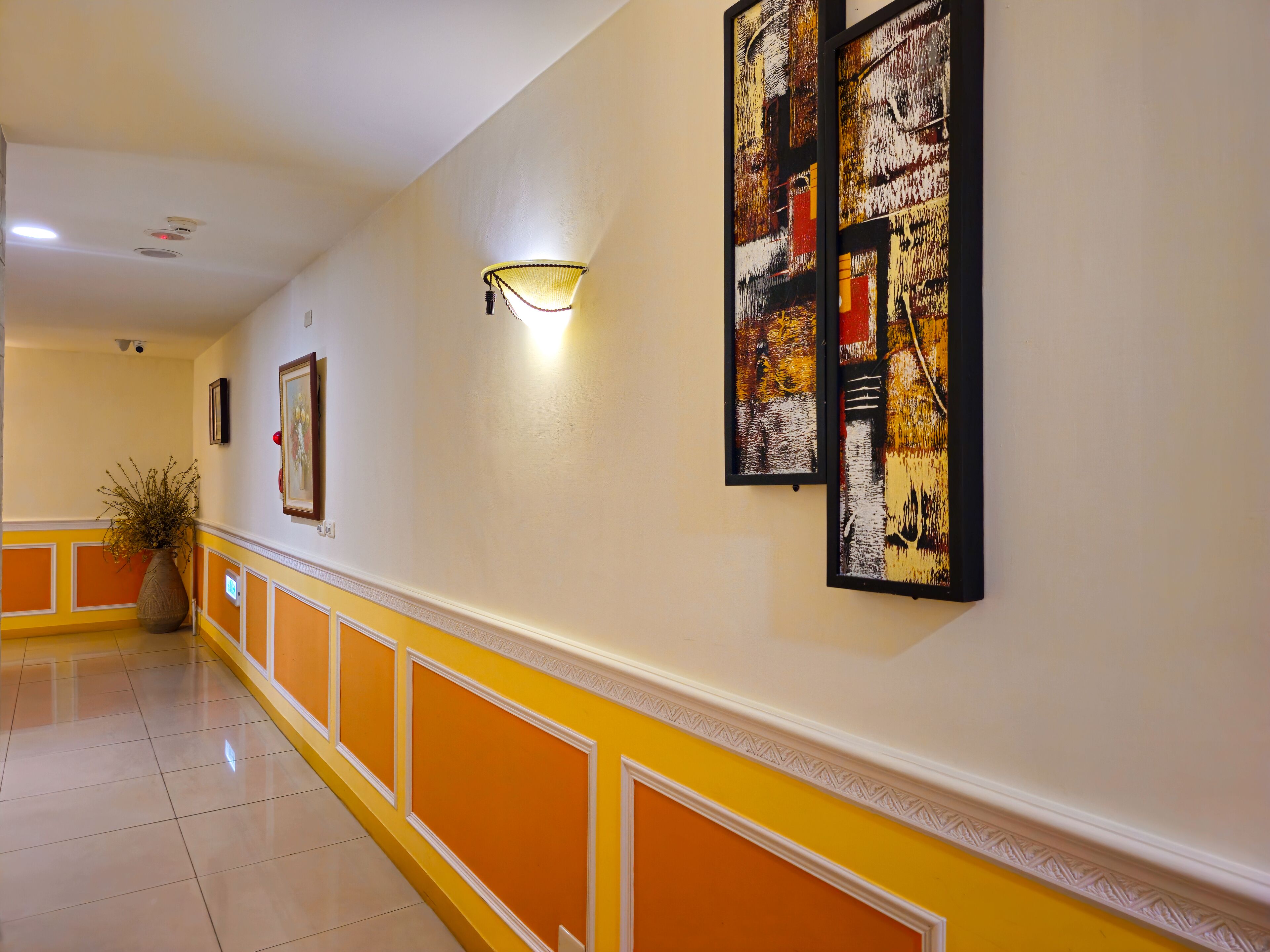 A hallway with yellow and white walls, a tiled floor, and framed artwork.